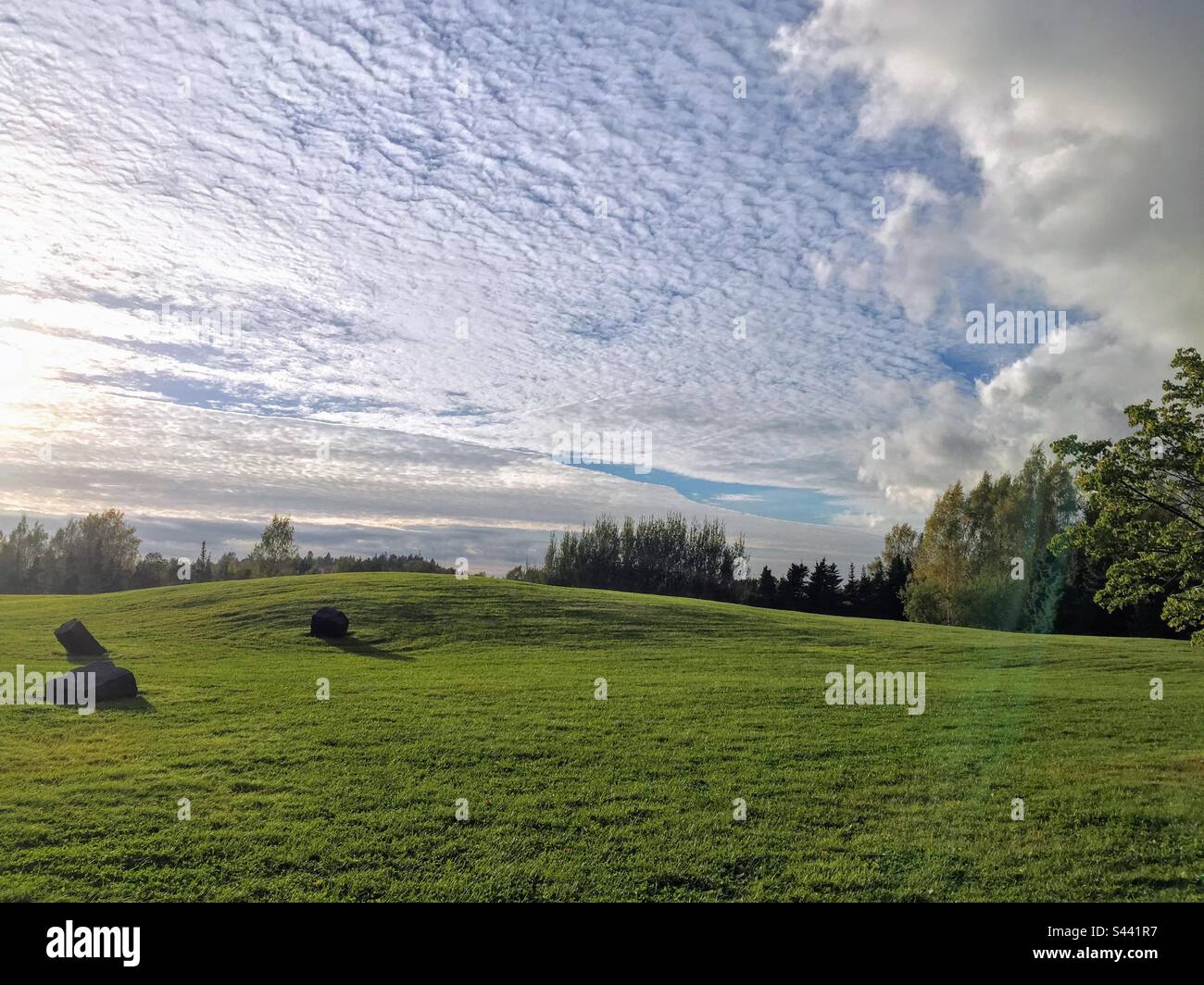 Beautiful tranquil landscape over green hill meadow with few stones under the cloudy sky with low sun light - Smartphone Captured Stock Image