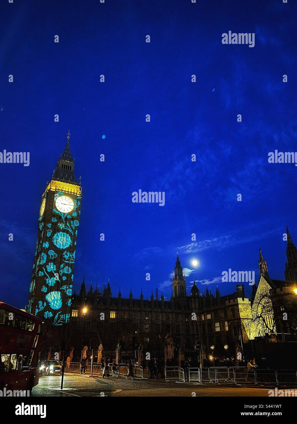Moon rises over an illuminated Houses of Parliament in London -illuminated with images of flowers representing countries of the United Kingdom celebrating coronation of King Charles III Stock Photo