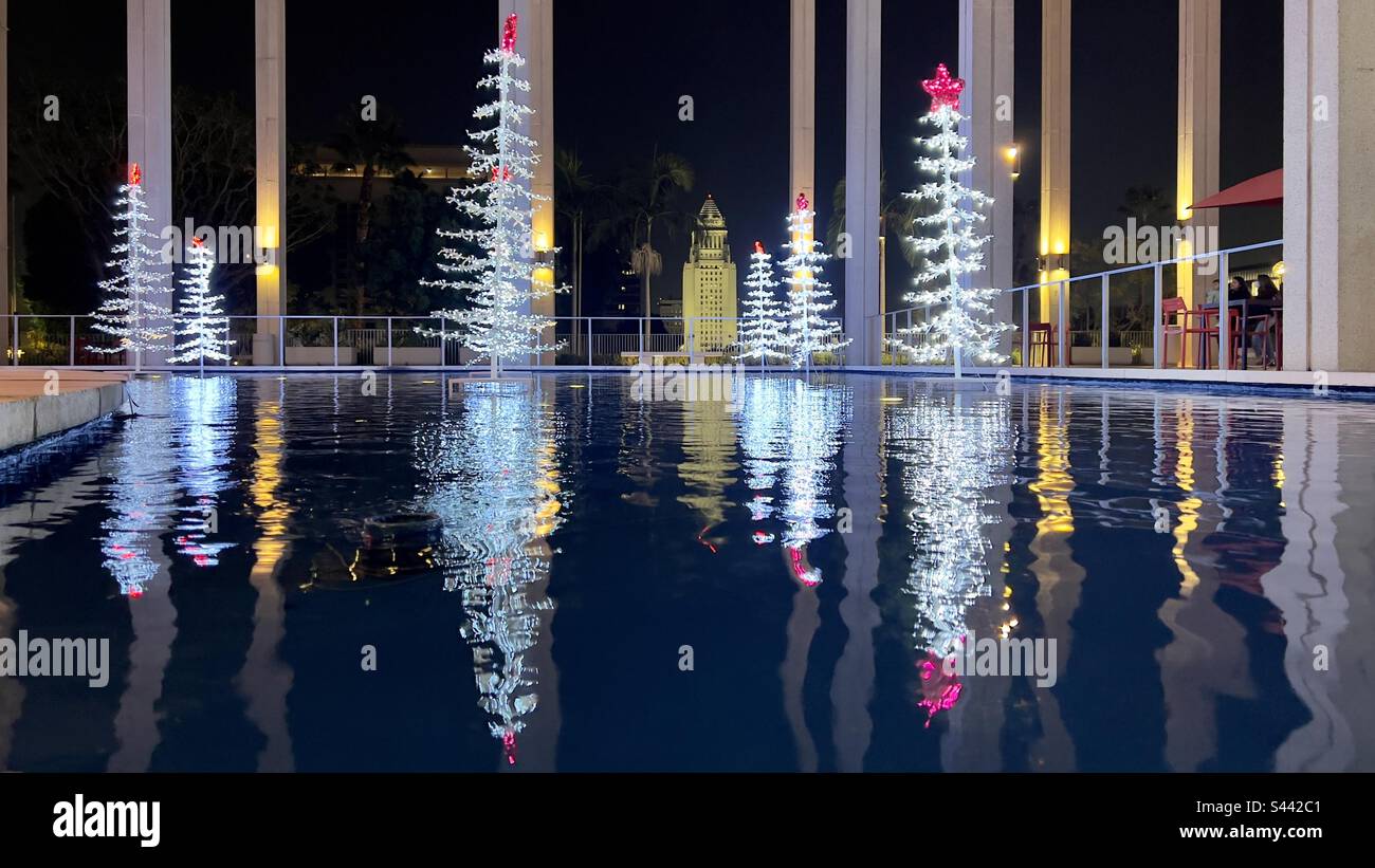 LOS ANGELES, CA, DEC 2022: wide view Christmas Trees decorated with white and red LEDs, with reflections in water at the Music Center in Downtown. City Hall in background, lit up at night - Smartphone Captured Stock Image