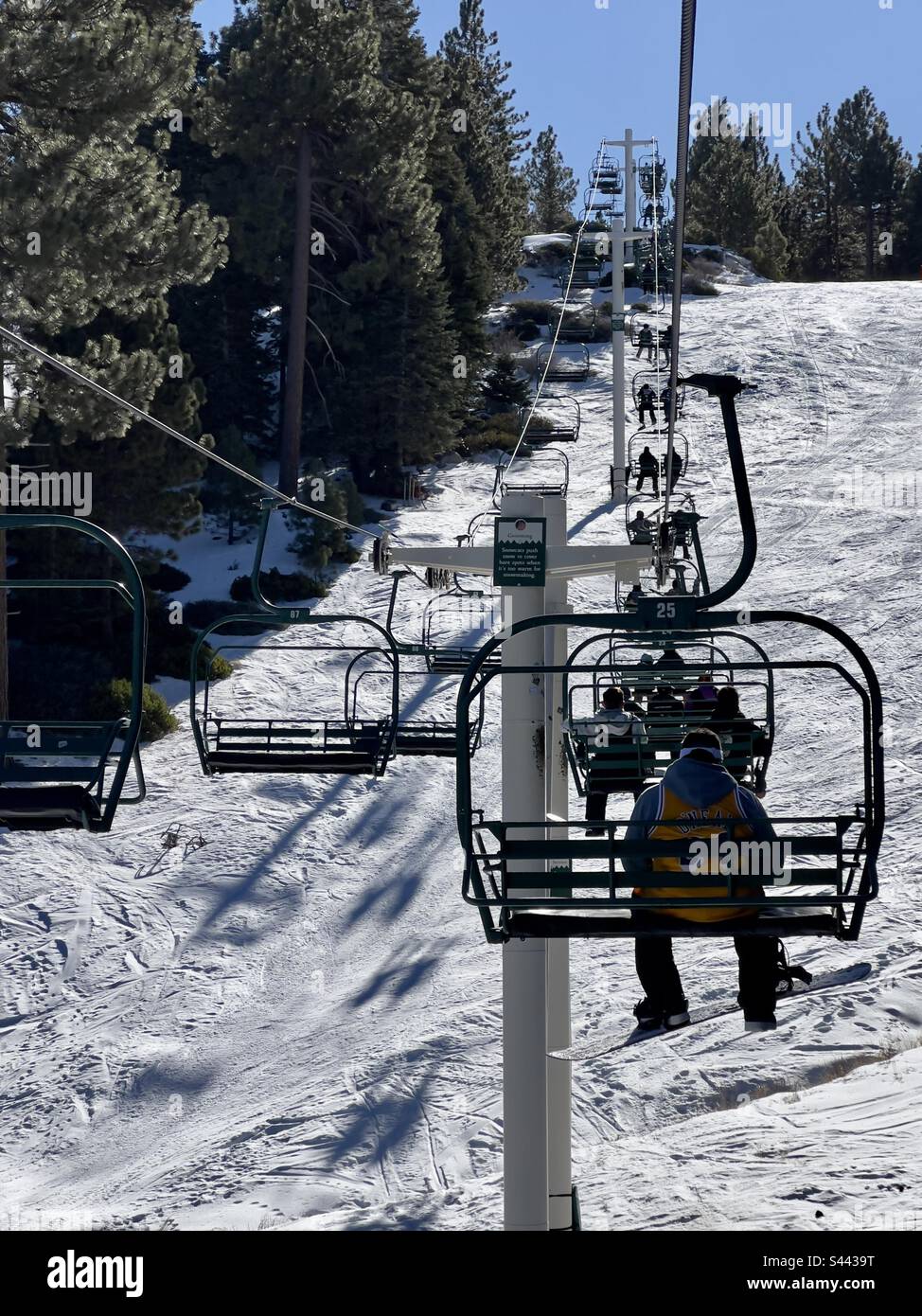 BIG BEAR, CA, DEC 2022: rear view, unidentified snowboarders and skiers on chair lift going up snow-covered mountain at Snow Summit, part of the Big Bear Mountain Resort - Smartphone Captured Stock Image
