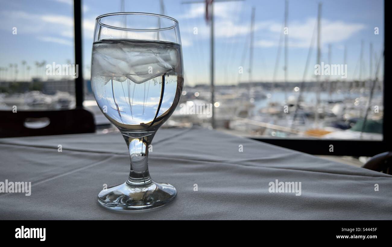 Glass of iced water with boat masts focused through it, and soft focus on yachts moored at Marina del Rey, California, in the background - Smartphone Captured Stock Image