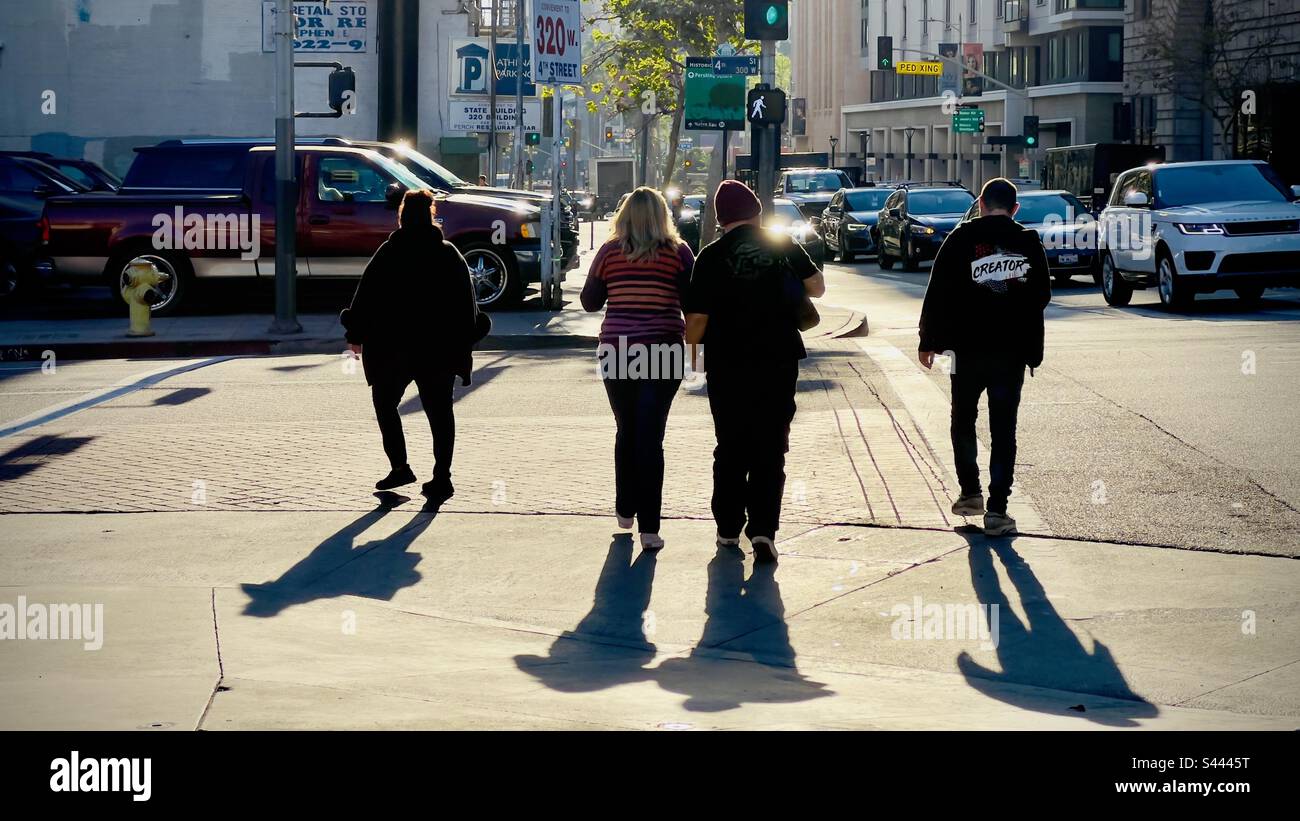 LOS ANGELES, CA, DEC 2022: anonymous pedestrians crossing road on Hill Street in Downtown, towards parking lot with traffic passing, low winter sun creates high contrast - Smartphone Captured Stock Image
