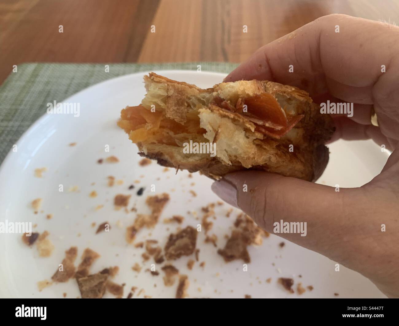 Woman holding a half eaten croissant filled with Parma ham and cheddar cheese above a white plate - Smartphone Captured Stock Image
