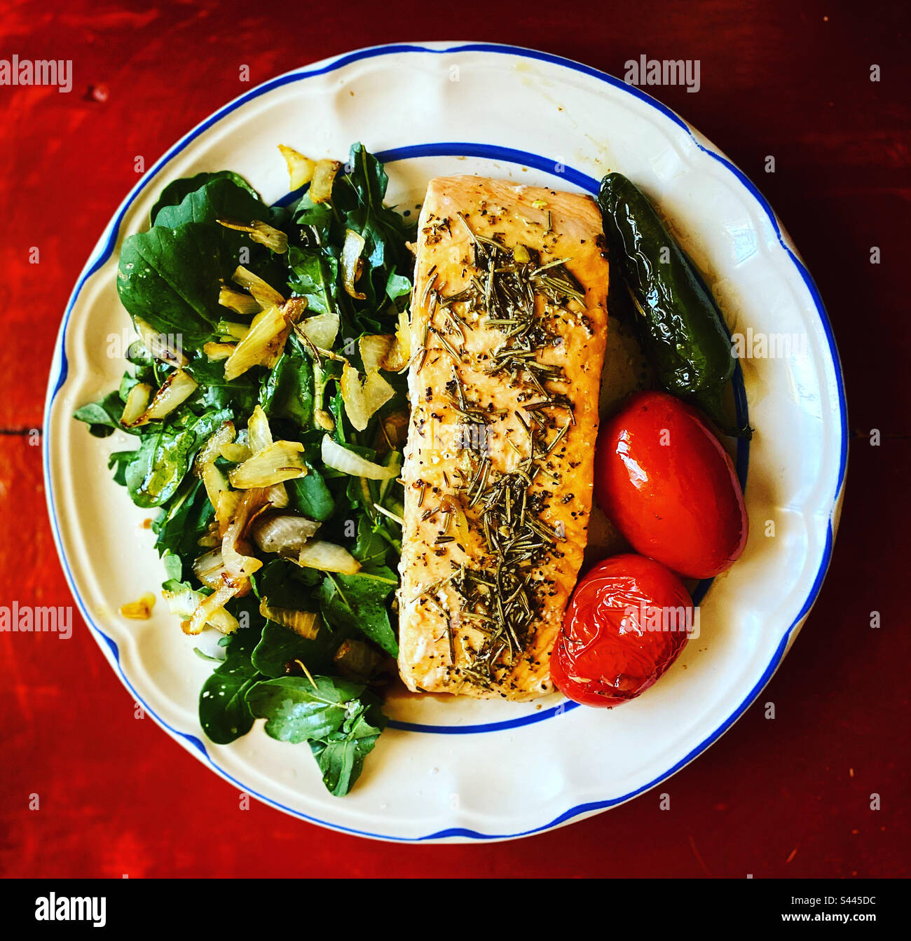 Ruccula salad with onion, a salmon fish piece with rosemary, two red tomatoes with a green hot chilli pepper in Queretaro, Mexico - Smartphone Captured Stock Image