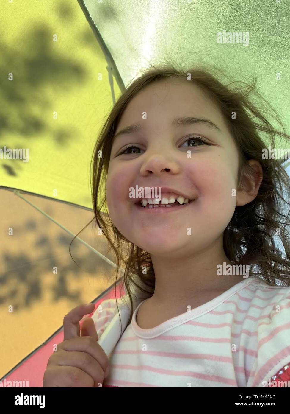 Smiling happy toddler girl under rainbow umbrella in summer sun. Stock Photo