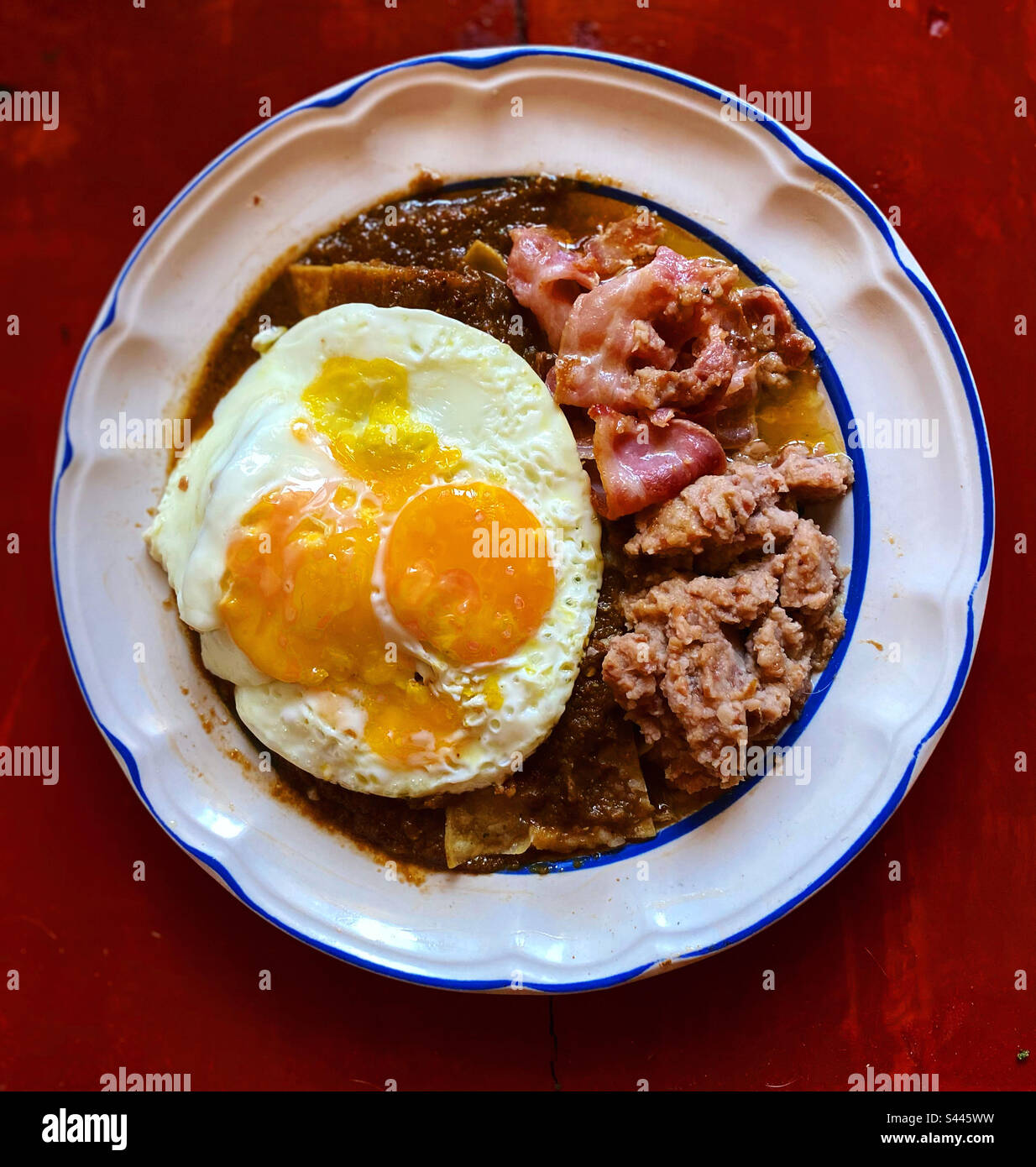 Chilaquiles rojos with fried eggs, bacon and beans in Queretaro, Mexico Stock Photo