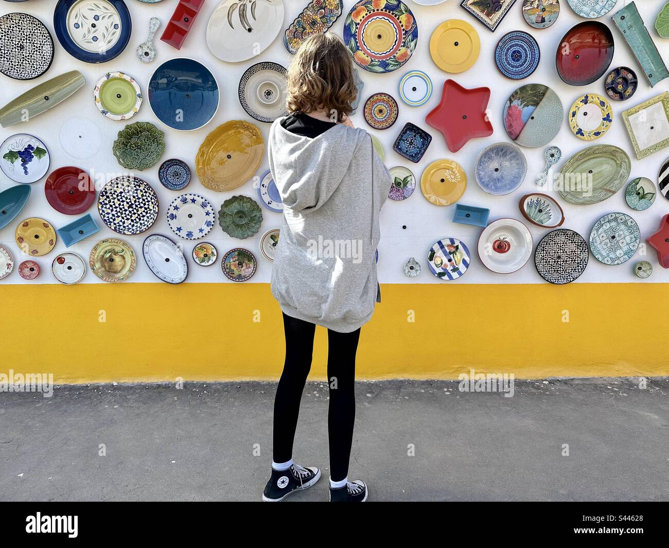 Teenage tourist looking at the plates hanging on the outside of a pottery shop in the Algarve - Smartphone Captured Stock Image