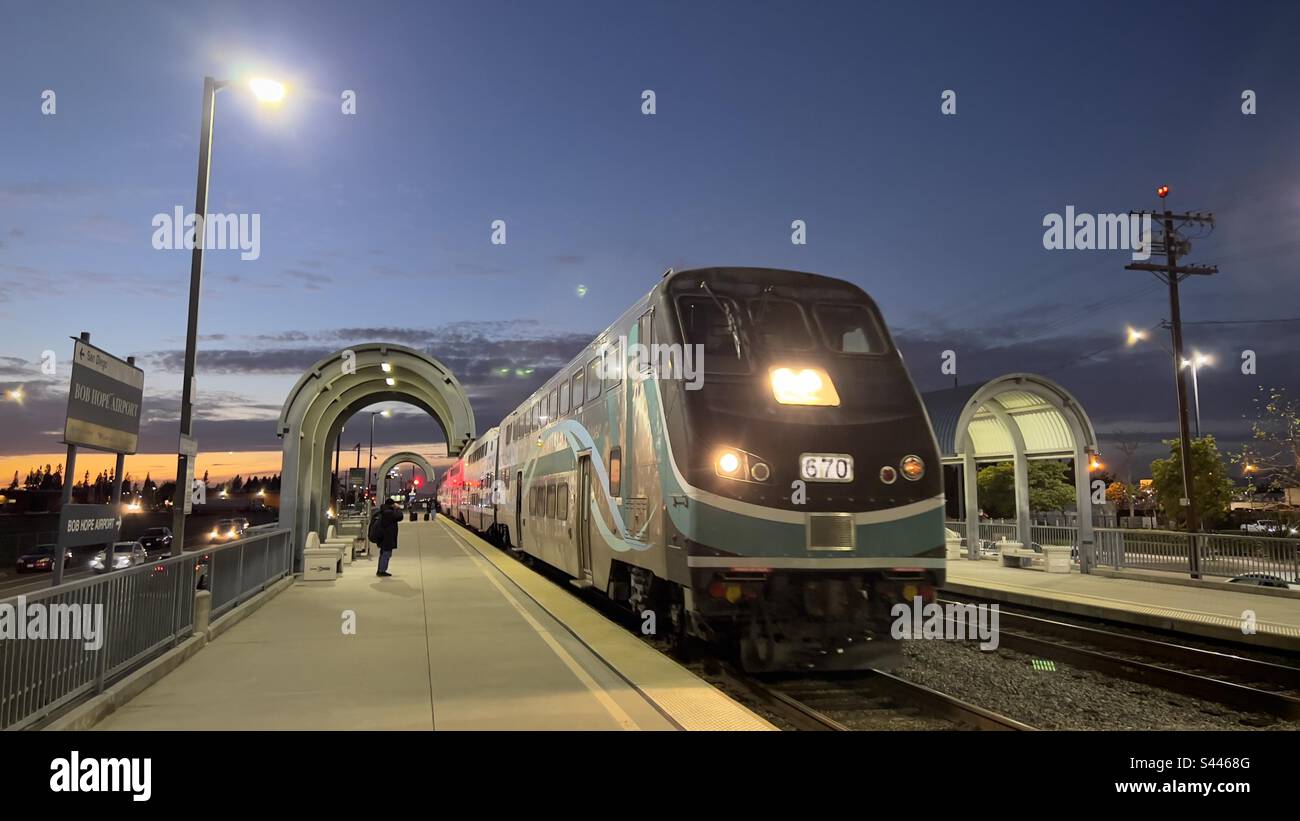 BURBANK, CA, DEC 2022: passengers wait on platform as Metrolink train arrives at light rail station at Burbank Airport, formerly known as Bob Hope Airport. Night time view - Smartphone Captured Stock Image