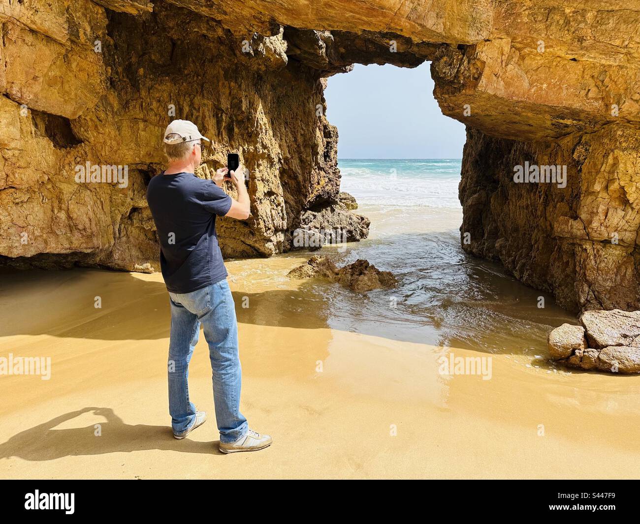 Tourist photographing a natural rock arch formation at Praia das Furnas beach in the Algarve - Smartphone Captured Stock Image