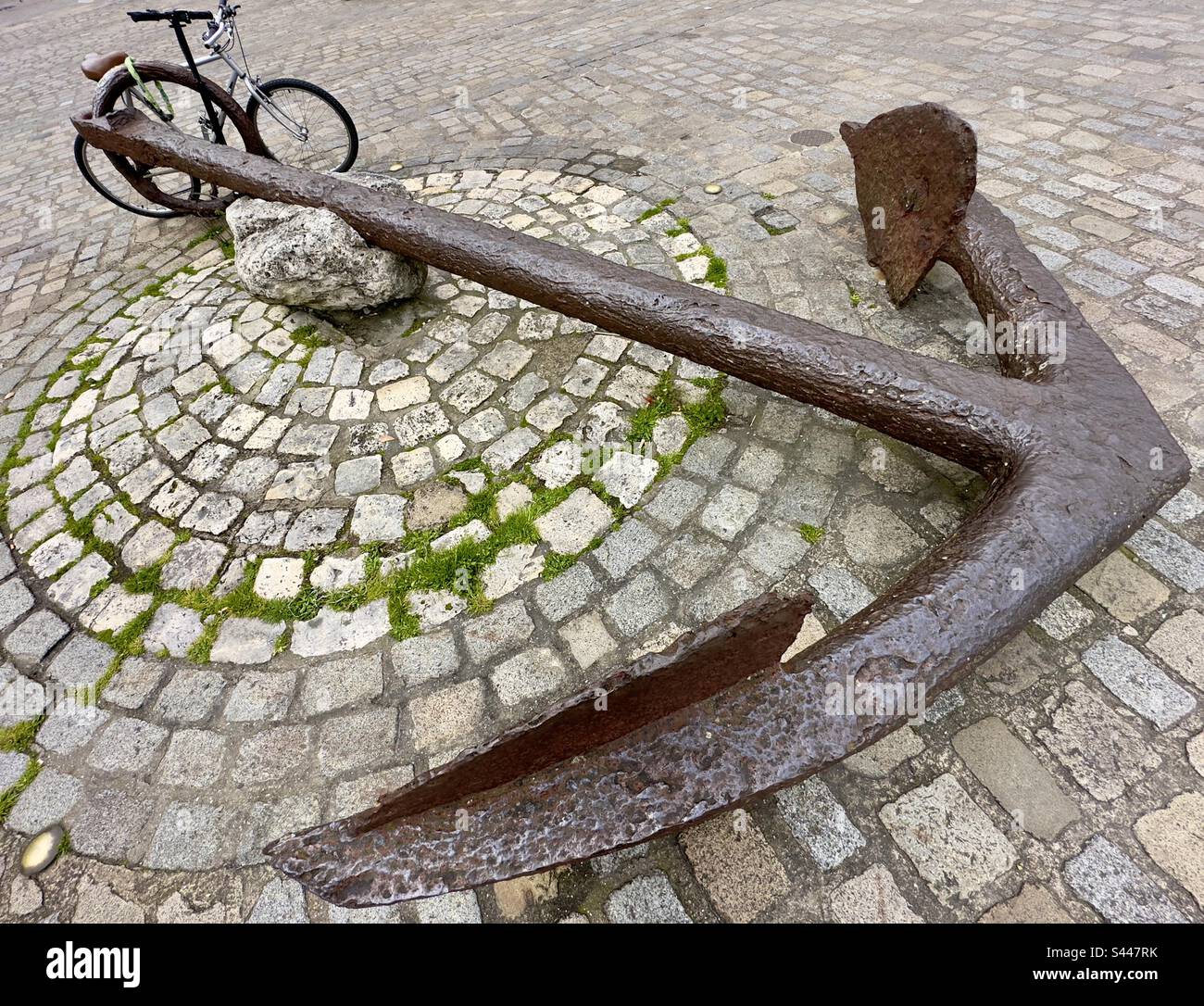 A huge wrought iron anchor resting on the cobbled quayside at La Rochelle in France, apparently securing a bicycle! - Smartphone Captured Stock Image