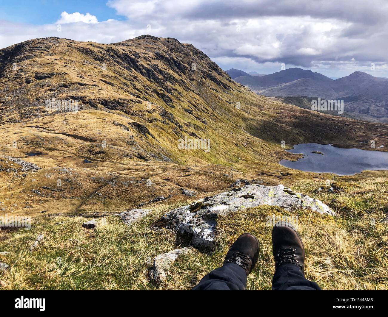 A Walker wearing a pair of leather boots on the slopes of Ben Oss with a view of Loch Oss and Beinn Dubhchraig, Tyndrum Scotland Stock Photo