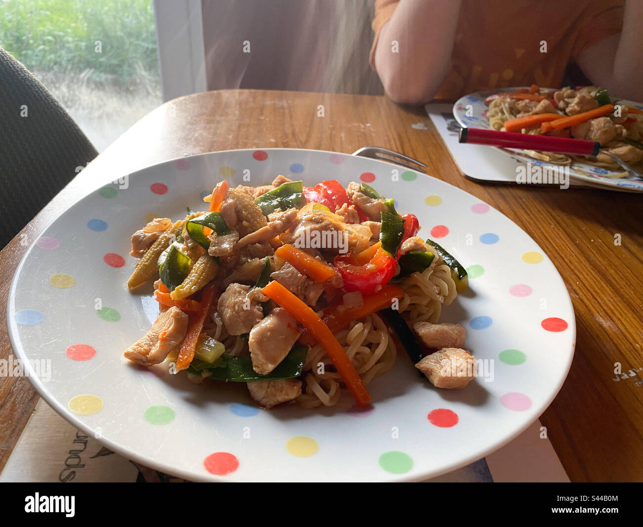 Steaming, homemade stir fried chicken with mixed vegetables served with egg noodles on a spotty plate. - Smartphone Captured Stock Image
