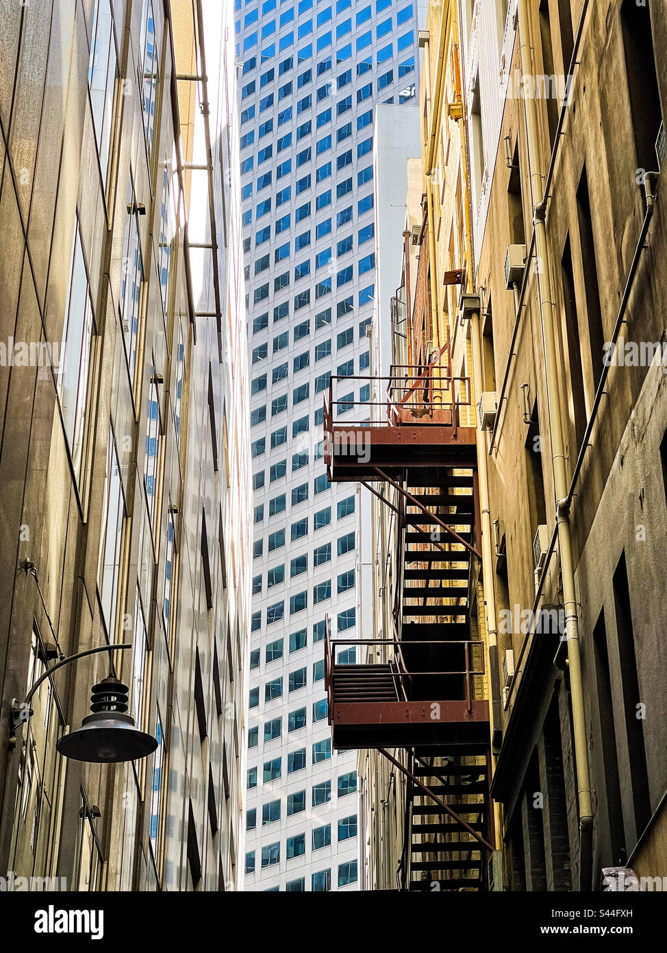 Juxtaposition. Old buildings with fire escape in narrow laneway against modern skyscraper in the middle at the end of the alley in Melbourne, Victoria, Australia. Low angle view. - Smartphone Captured Stock Image