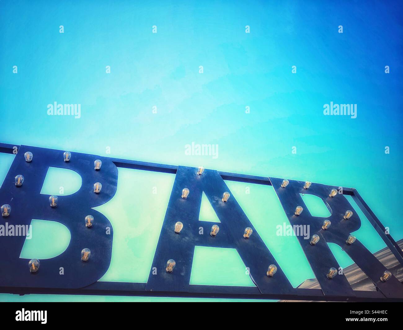 A photograph of a ‘bar’ sign with lightbulbs. Festival decor with blue sky and copy space - Smartphone Captured Stock Image