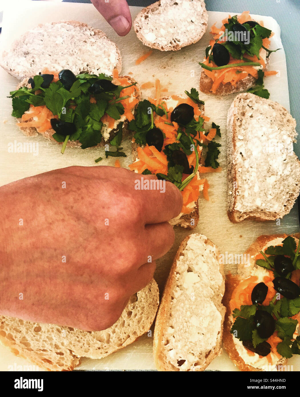 Vegan Sandwiches: Hands Making Houmous, Grated Carrot, Black Olive and Coriander Sandwiches on Sourdough Bread. Stock Photo