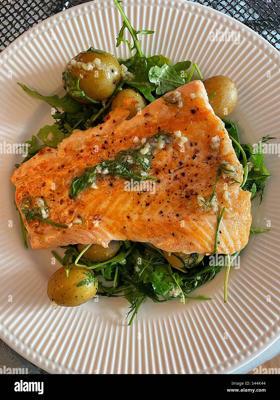 Close up of a broiled salmon fillet on a bed of arugula and new potatoes covered in a dill garlic lemon sauce, 2023, USA - Smartphone Captured Stock Image