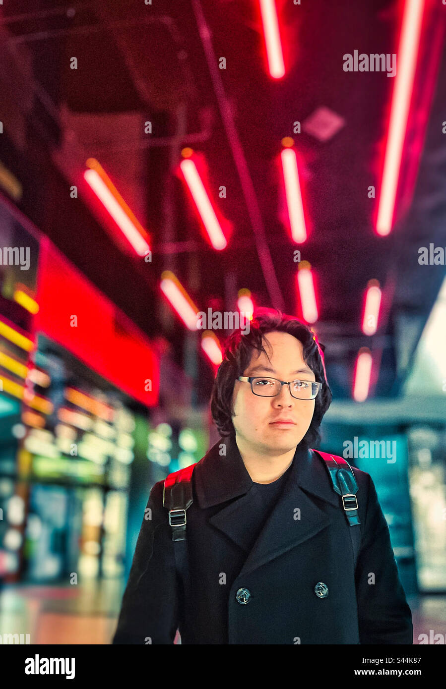 Portrait of young Asian man standing against multicolored neon lights in the city at night. - Smartphone Captured Stock Image