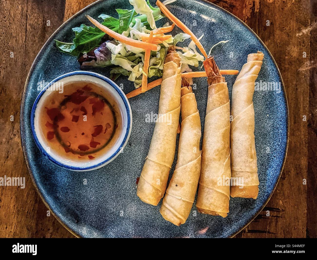 Directly above view of four crispy prawns encased in pastry wrappers together with fresh salad and chili dip on plate on table. Lumpia. Spring rolls. - Smartphone Captured Stock Image