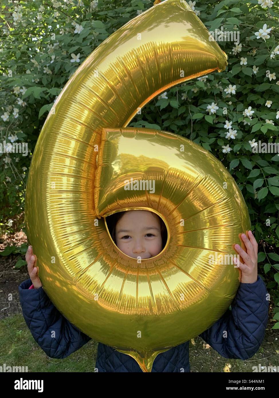 Little girl cheekily holding 6th birthday balloon. Stock Photo