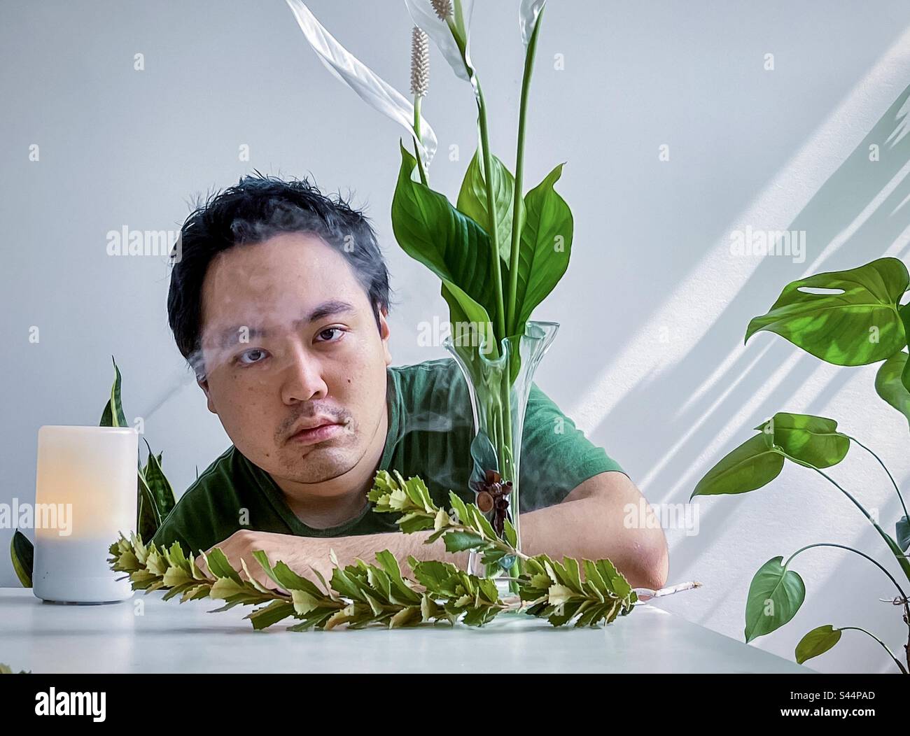 Young Asian man creating soothing, natural ambiance in the home using aromatherapy diffuser, essential oils and flower arrangement. Self care. Well-being. Alternative therapy. - Smartphone Captured Stock Image