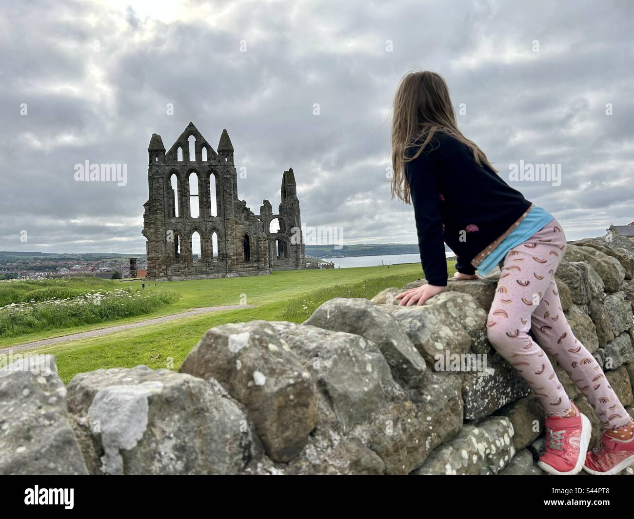 Whitby Abbey with a rear view of a girl climbing over the stone wall to see - Smartphone Captured Stock Image