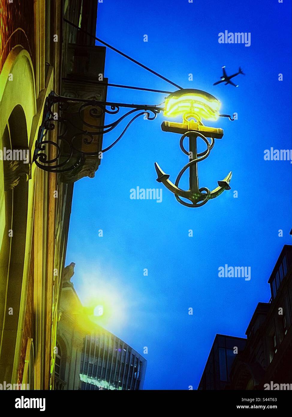 Anchor sign above a building in the city of London - an aeroplane flies in the night sky. - Smartphone Captured Stock Image Anchor sign above a building in the city of London - an aeroplane flies in the night sky. - Smartphone Captured Stock Image