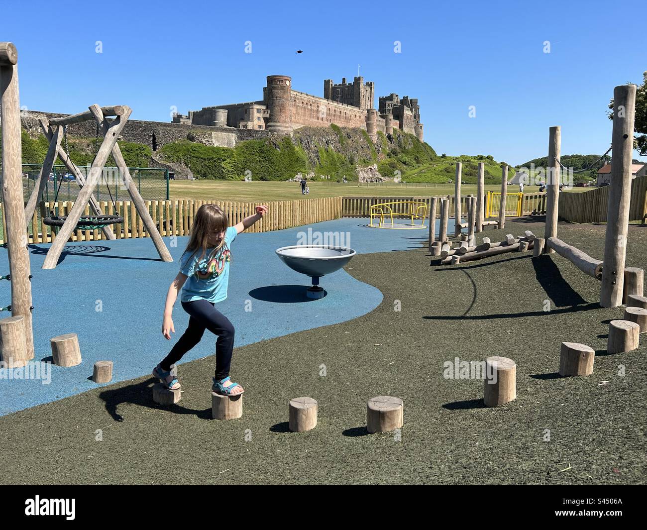 Girl balancing on play park equipment in front of Bamburgh castle, Northumberland - Smartphone Captured Stock Image