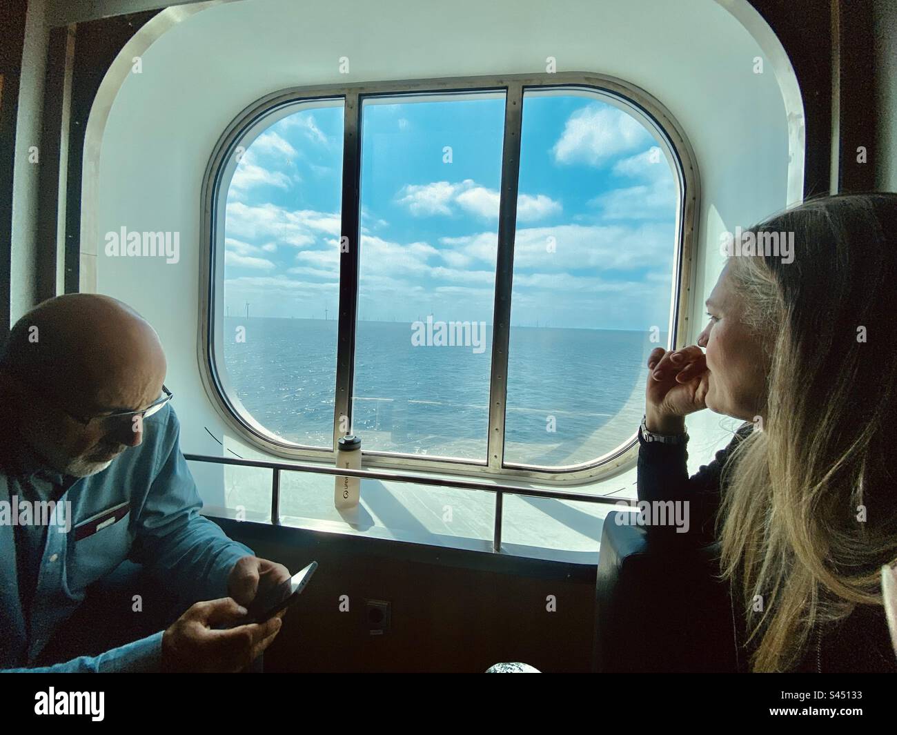 Two people relax by the window of a ferry during a crossing to Europe Stock Photo
