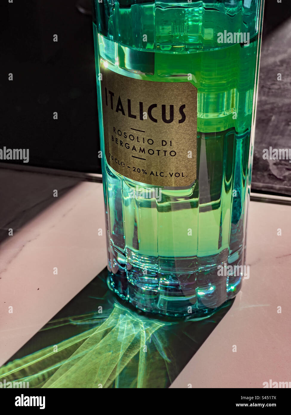 Bottle of Italicus Rosolio di Bergamotto liquer with evening sun shining through from behind and creating a light pattern on the table surface Stock Photo