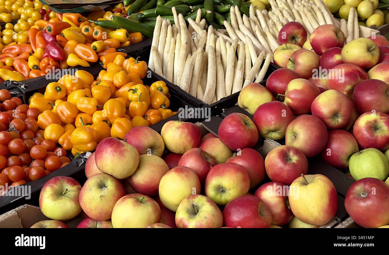 A greengrocery stall in the street market at Lieden displaying fruit and vegetables, including apples, yellow peppers, and white asparagus - Smartphone Captured Stock Image