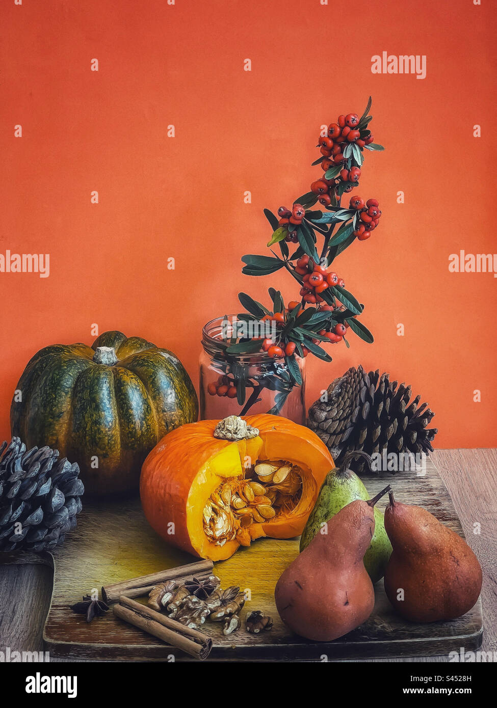 Still life of arrangement of pumpkins, pine cones, pears, walnuts, spices and orange Cotoneaster berry branches against orange background. Autumn. Thanksgiving. Celebration. Stock Photo