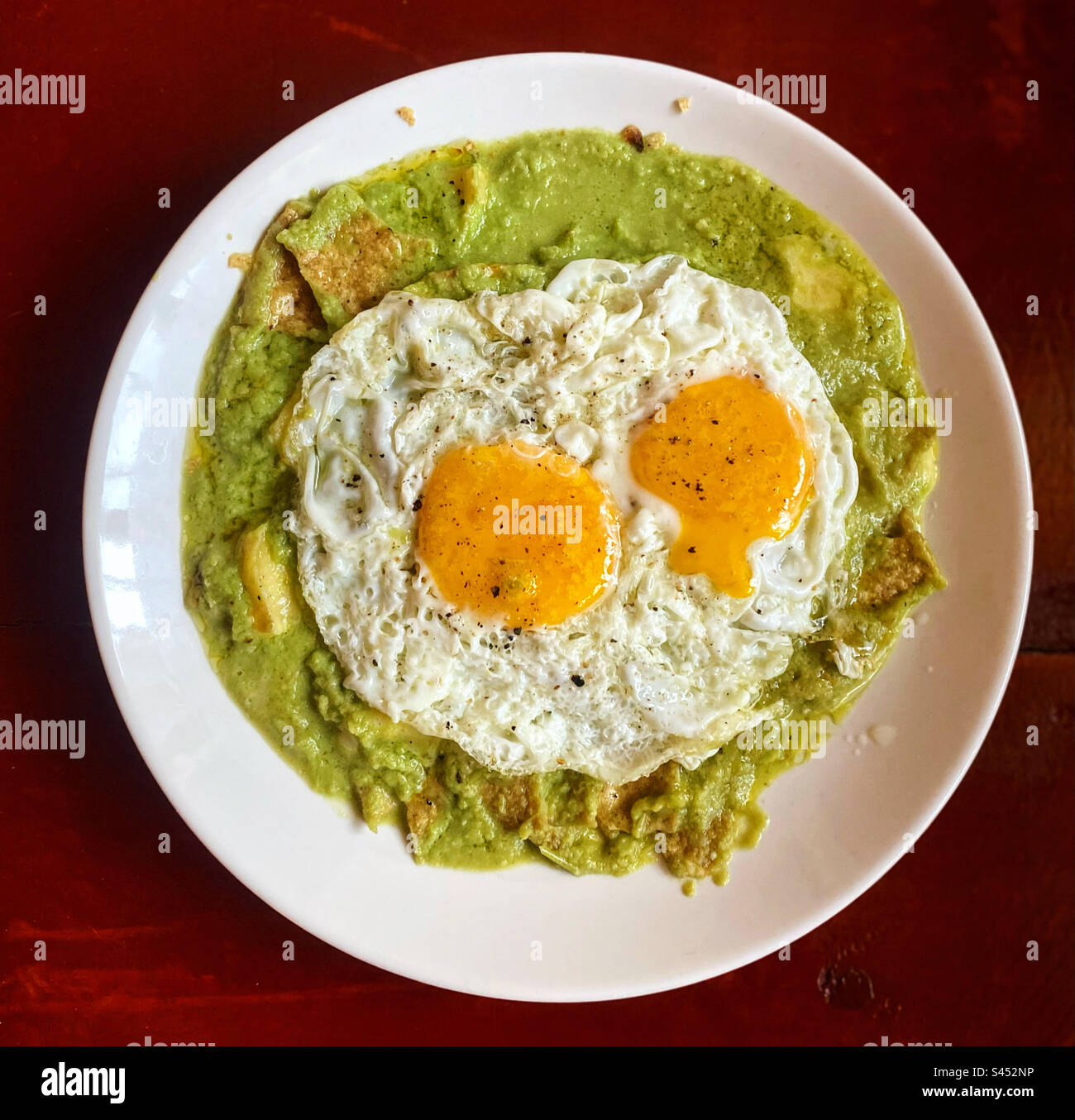 Two eggs on top of chilaquiles verdes with green tomatoe sauce for breakfast in Queretaro, Mexico Stock Photo