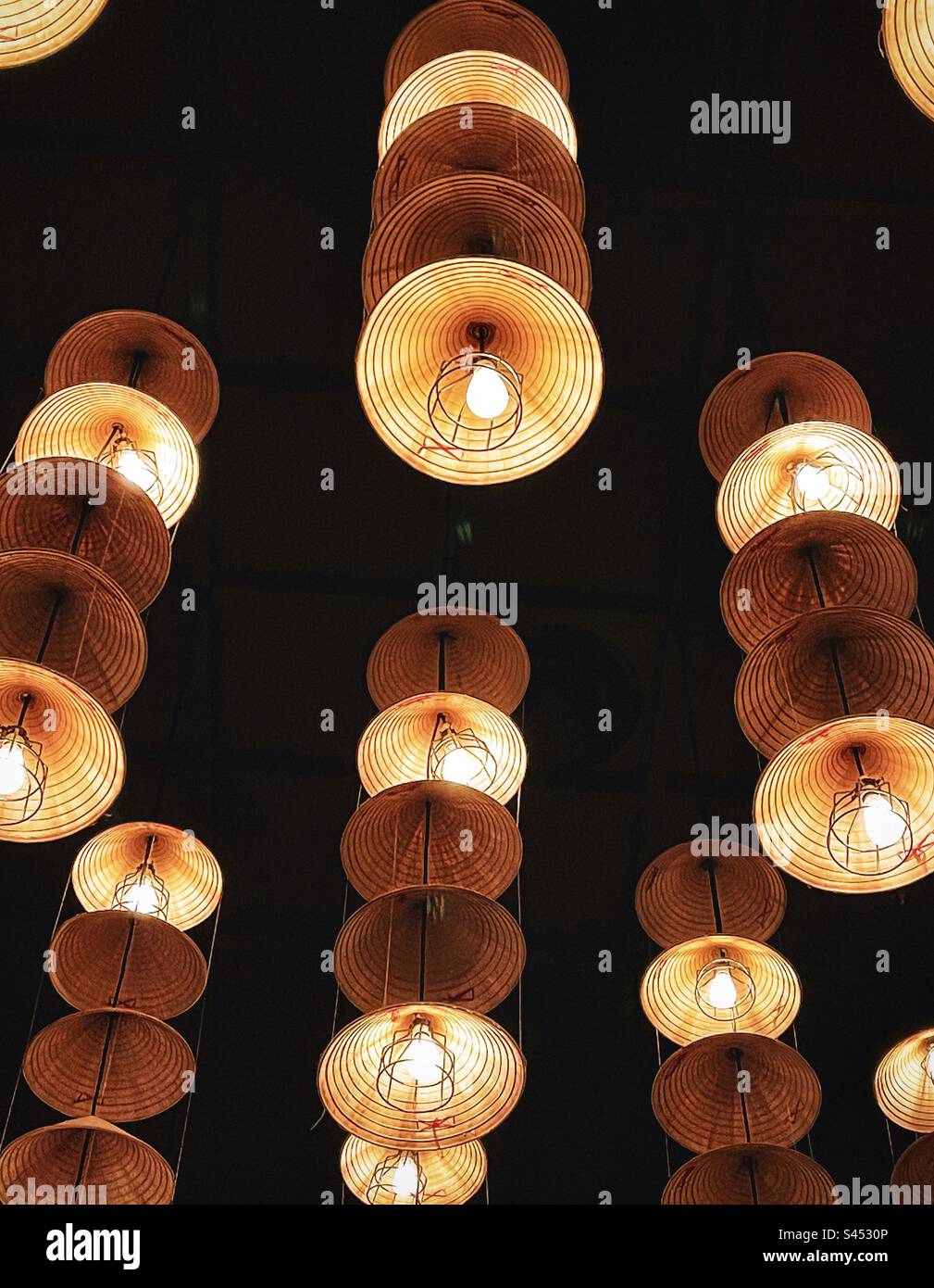 Low angle view of rows of multiple straw hat pendant lights hanging from ceiling. - Smartphone Captured Stock Image