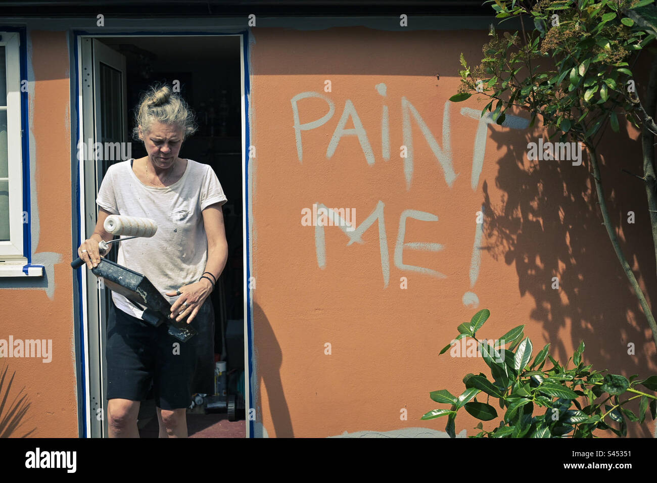 A woman prepares to paint a new colour on an outbuilding in the UK - Smartphone Captured Stock Image