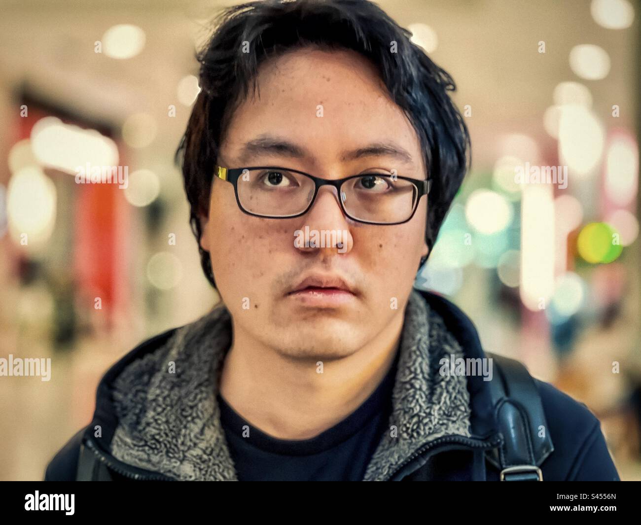 Close-up portrait of young Asian man in eyeglasses against illumination and bokeh background. Focus on foreground. - Smartphone Captured Stock Image