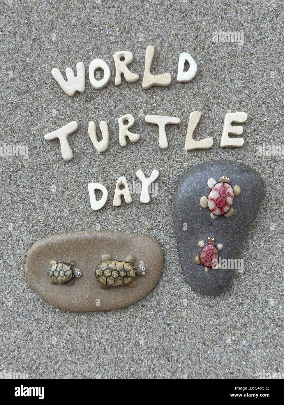 World turtle day celebrated with wooden letters and artistic stones and pebbles over brown sand - Smartphone Captured Stock Image