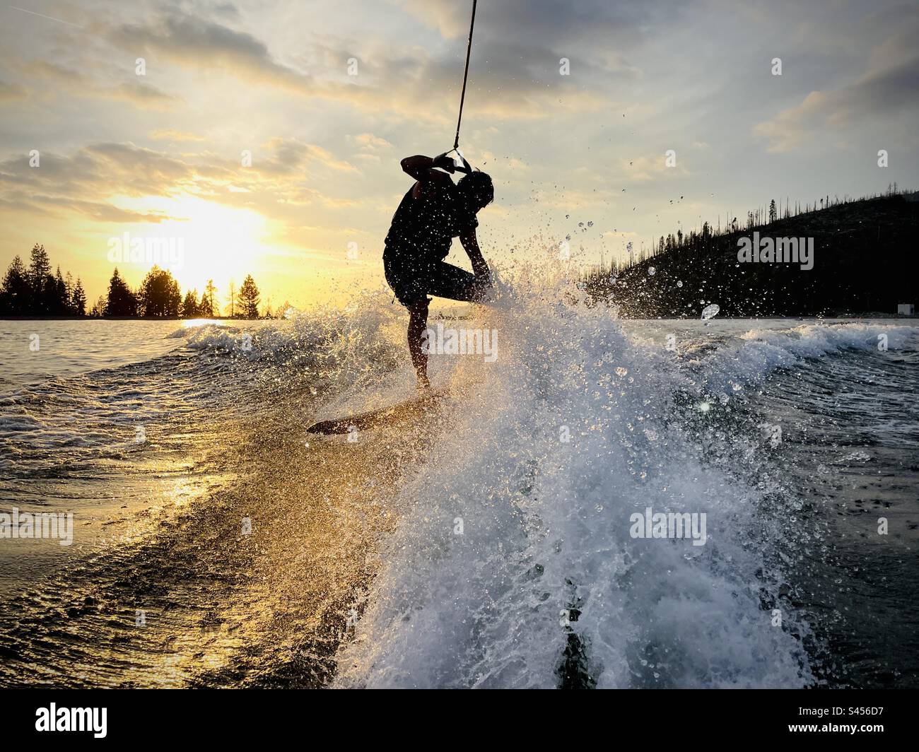 Male wakeboarder does a turn on the lake at sunset. Shaver Lake, California USA. Stock Photo