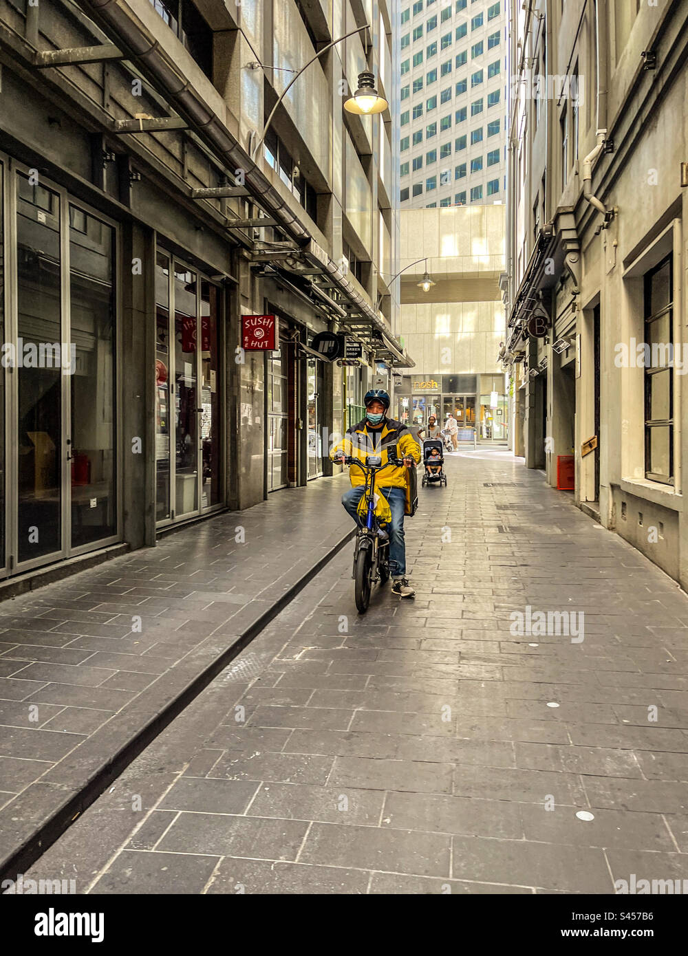 Food delivery man riding electric bicycle in laneway in Melbourne, Victoria, Australia. Food delivery services using e-bikes. - Smartphone Captured Stock Image