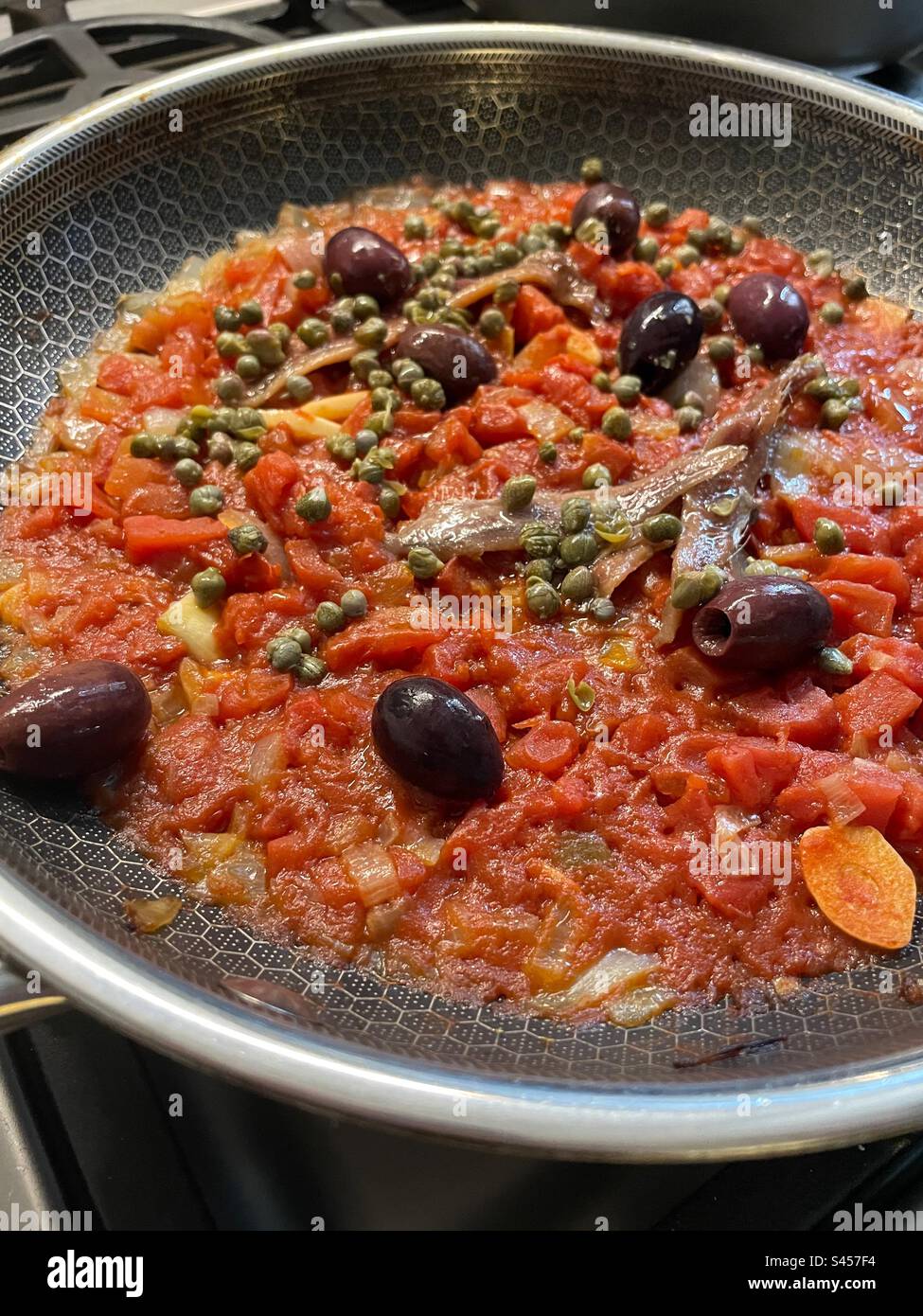 Stove top close-up of puttanesca sauce sautéing in a skillet in a residential kitchen, 2023, USA - Smartphone Captured Stock Image Stove top close-up of puttanesca sauce sautéing in a skillet in a residential kitchen, 2023, USA - Smartphone Captured Stock Image