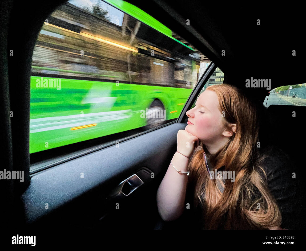 Young women looking out of car window while green bus passing by - Smartphone Captured Stock Image