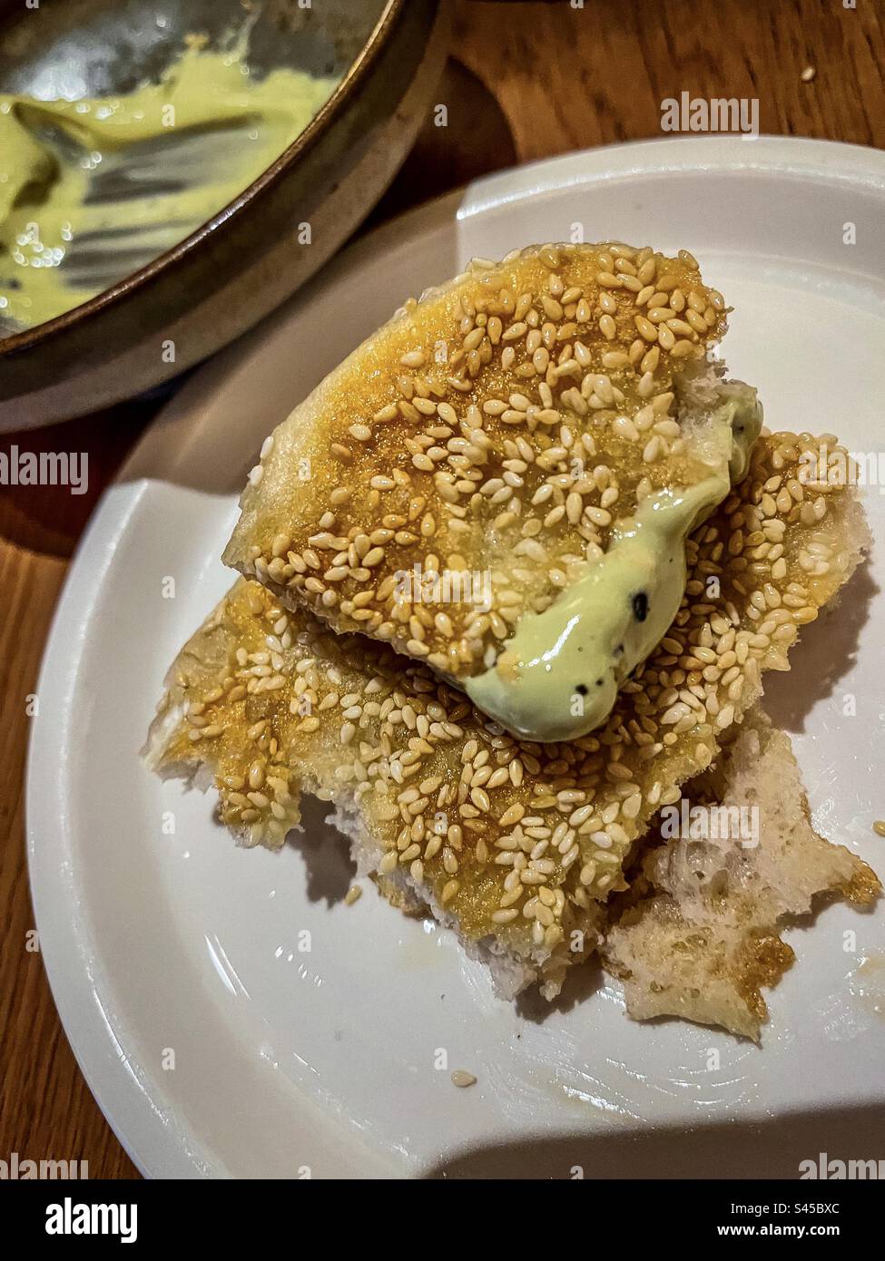 Close-up of partially eaten sesame flatbread with creamy avocado dip on plate on table. - Smartphone Captured Stock Image