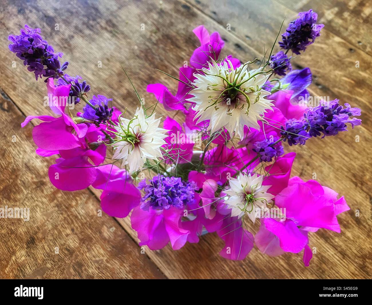 Small bouquet of pink sweet peas, purple lavender and white love in a mist flowers in a vase on a wooden table, from above - Smartphone Captured Stock Image