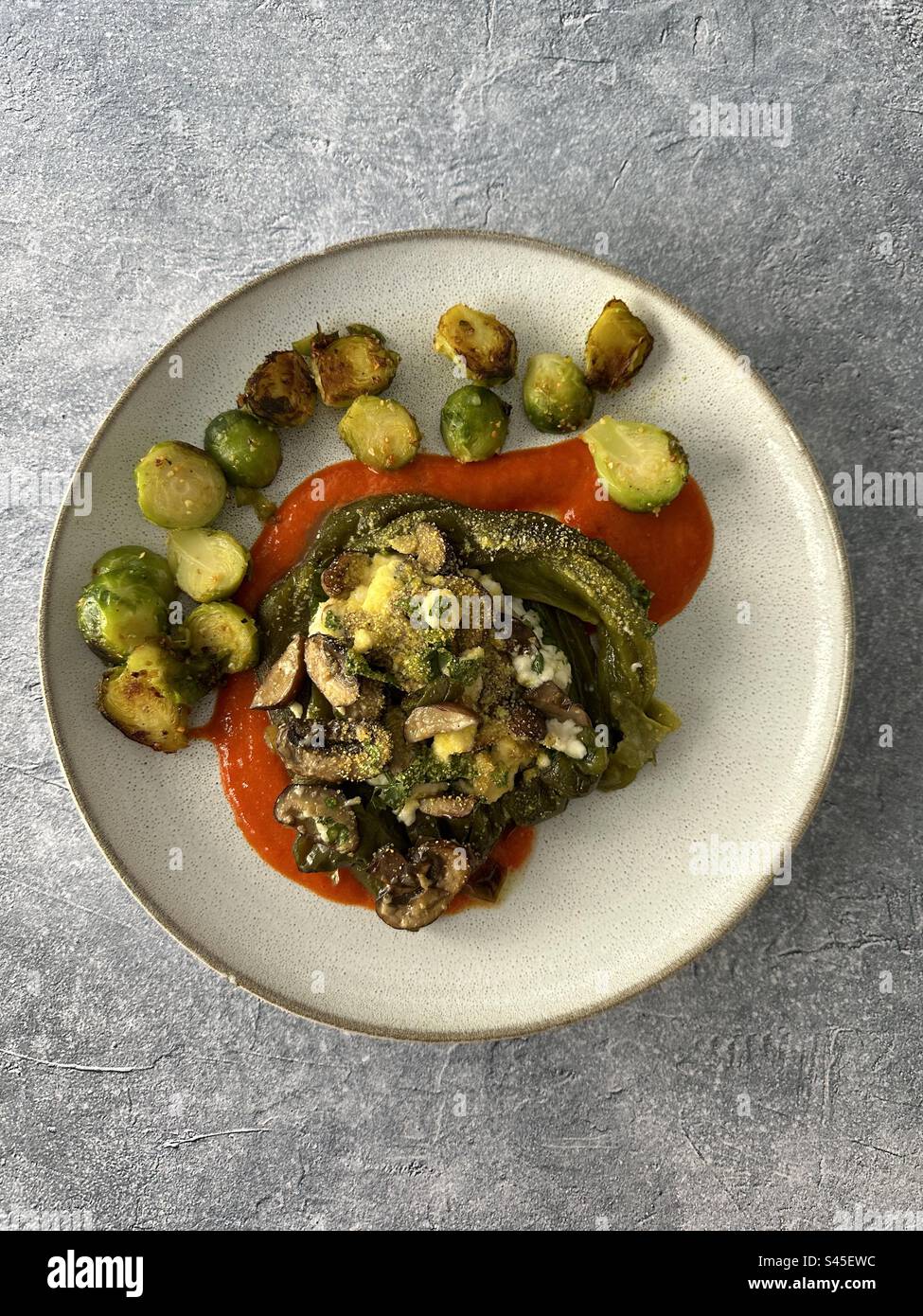 Green bell pepper stuffed with mushrooms and goat cheese, roasted peppers sauce and Brussels sprouts Stock Photo