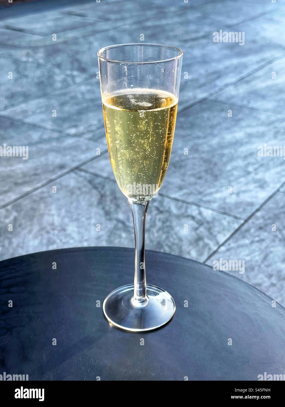 Flute glass of champagne on a table on a garden patio. No people. Stock Photo