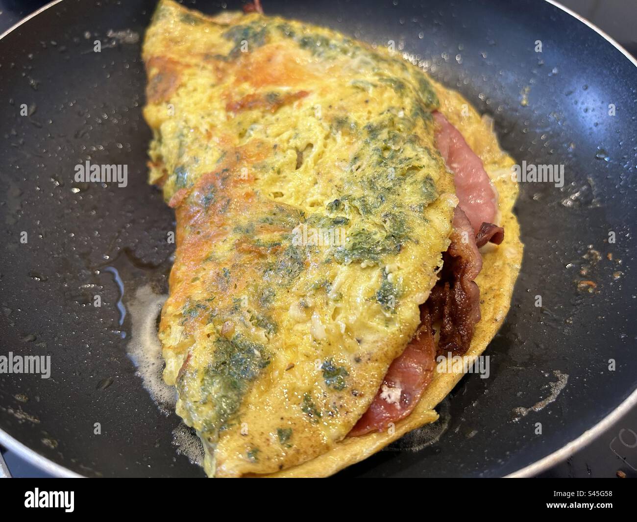 Omelette with herbs and cheese, stuffed with crispy bacon. Stock Photo