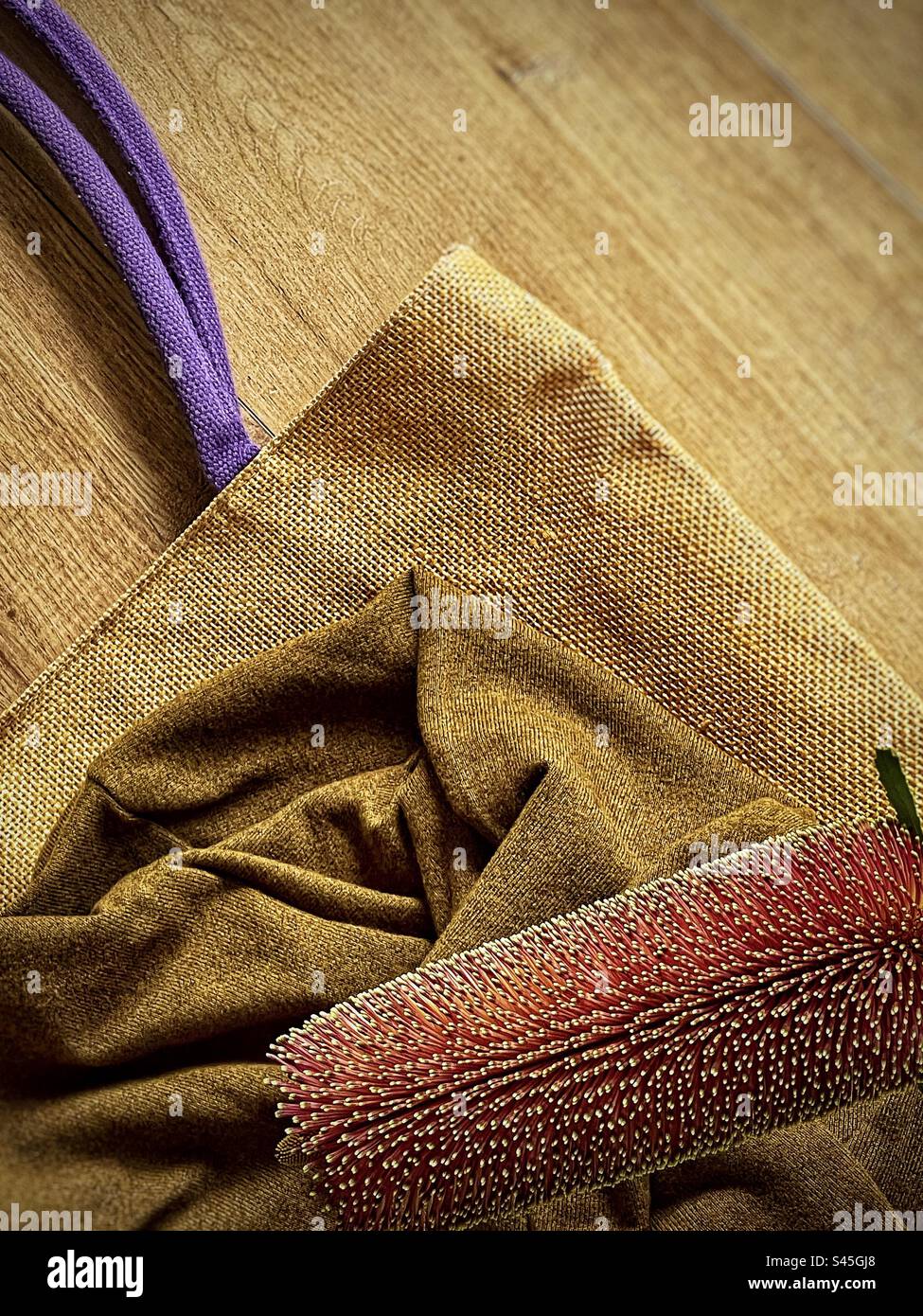 High angle view of banksia flower and brown jumper on straw bag on wood. Fashion. Textile. Art. Natural fibers. - Smartphone Captured Stock Image