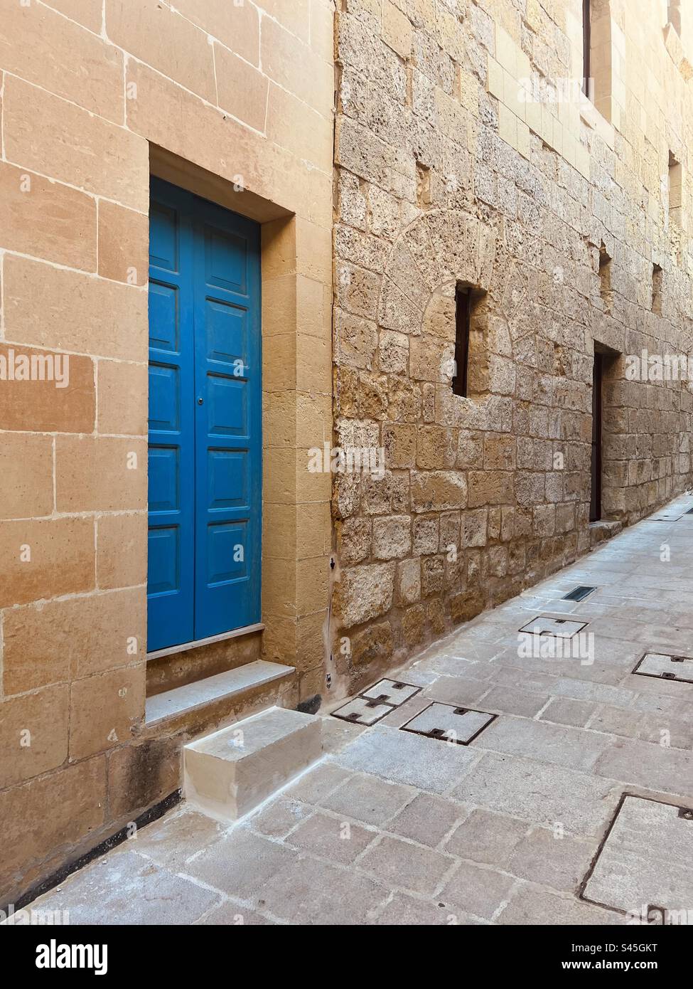 New limestone blocks facade with beautiful traditional Maltese blue entrance doors versus old stone facade in the old town citadel on the Gozo island, Malta - Smartphone Captured Stock Image