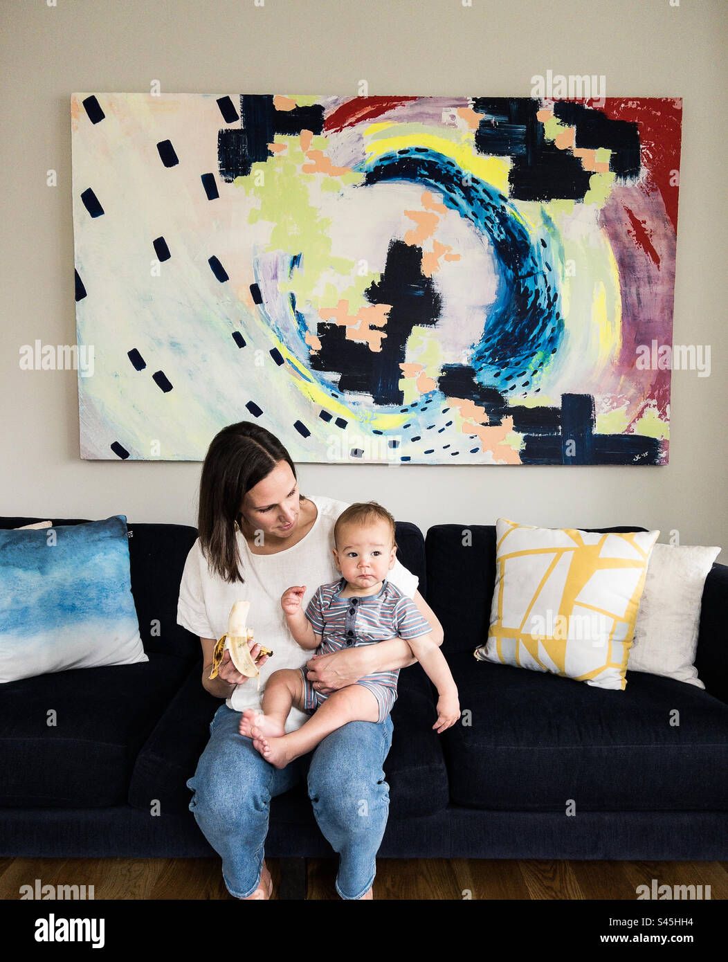 Mother and son eating a banana in front of a colorful piece of art Stock Photo