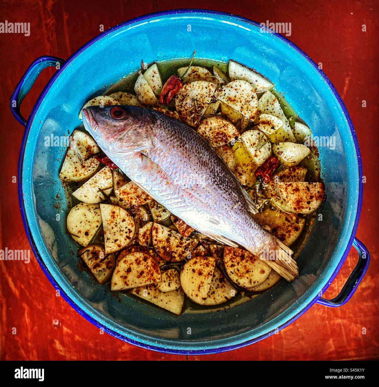 A red snapper fish on top of potatoes with pimiento de la vera chilli peppers and fine herbs ready to be grilled in Queretaro, Mexico - Smartphone Captured Stock Image