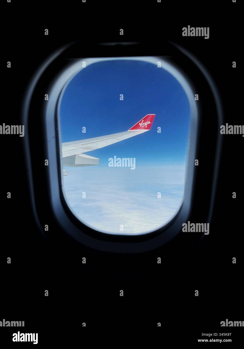 Wing tip of a Virgin Atlantic Airways jet at cruising altitude with the view framed by the aircraft window. Stock Photo